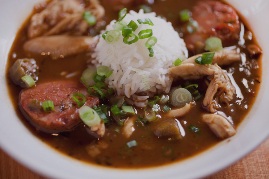 Close up view of bowl of gumbo with a dollop of white rice in the middle and topped with green onions